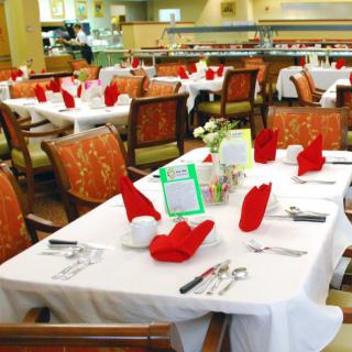 A well-arranged restaurant dining area with tables set elegantly, featuring red napkins and neatly placed utensils.