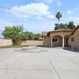 A sunny day in a residential area with a house featuring an arched porch and a spacious concrete driveway.