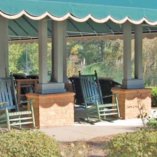 A shaded gazebo with rocking chairs overlooking a garden area.