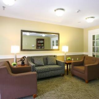 A cozy living room featuring a sofa, armchairs, and a coffee table arranged around a carpet with soft indoor lighting.