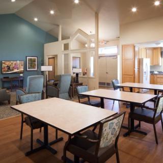 A spacious dining area with tables and chairs, featuring wooden flooring and an open kitchen.