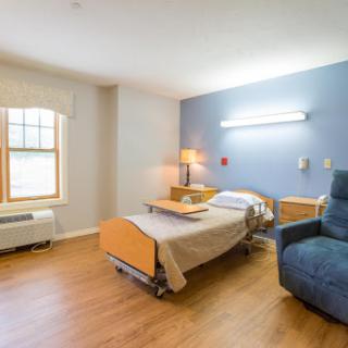A well-lit and clean hospital patient room featuring a bed, chair, and window.