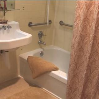 A bathroom with a sink, bathtub, and shower curtain, equipped with grab bars for safety.