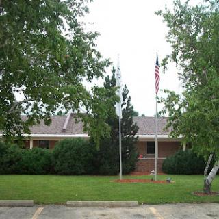 A view of a single-story building with flags displayed in front, surrounded by greenery.