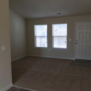 An empty room with carpet flooring, two windows, and a door.