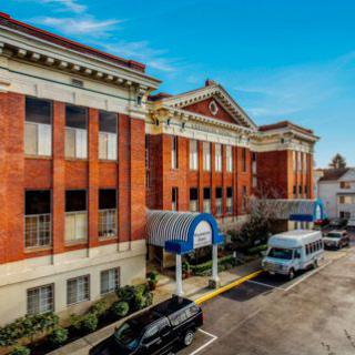 A historic hospital building with classic architecture, featuring parked vehicles along the adjacent street.