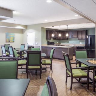 A well-lit dining area with green upholstered chairs and a modern kitchen in the background.