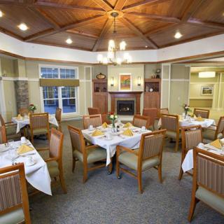 An elegantly decorated dining room featuring neatly arranged tables and chairs, a chandelier, and a cozy fireplace.