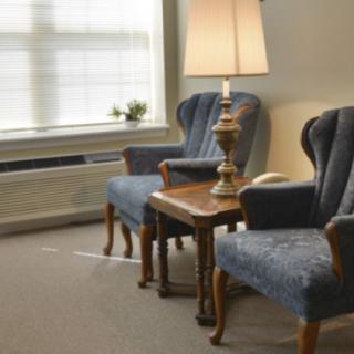 A cozy sitting area with two blue armchairs and a wooden table topped by a lamp.