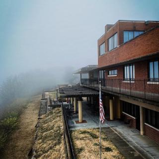 A brick building stands on a foggy day, with an American flag in the foreground.