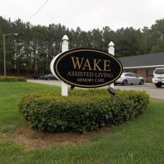 Sign for Wake Assisted Living facility with building and landscaped area in the background.
