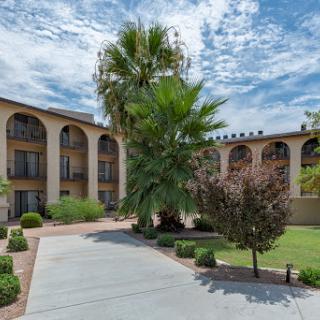 A beautifully designed hotel surrounded by lush landscaping and palm trees under a partly cloudy sky.