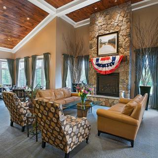 A spacious living room featuring a stone fireplace, leather sofas, and decorative armchairs under a wooden ceiling.