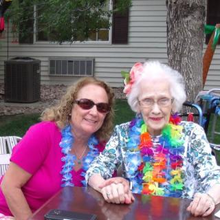 Two women enjoying an outdoor party, wearing colorful leis and smiles.