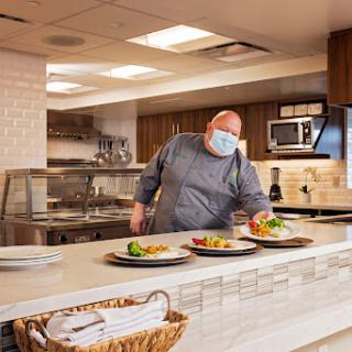 A chef plates dishes in a modern kitchen while wearing a mask.
