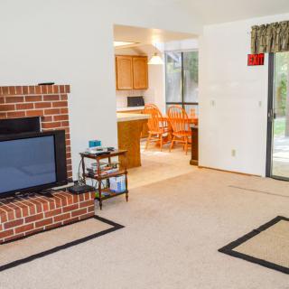 A cozy living room with a brick fireplace, television, and view into the kitchen area.
