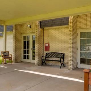 A building entrance with a brick wall features outdoor benches and a covered patio area.