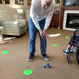 An elderly man practicing putting golf indoors, surrounded by markers for guidance.