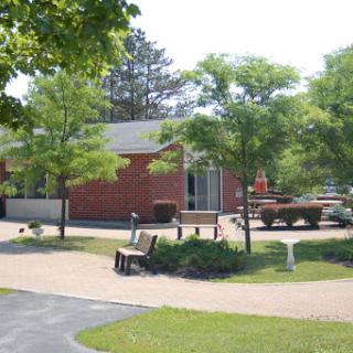 A serene park setting featuring a brick building surrounded by lush trees and a paved pathway.