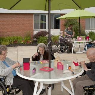 A group of seniors enjoying a social gathering outdoors under umbrellas on a patio.