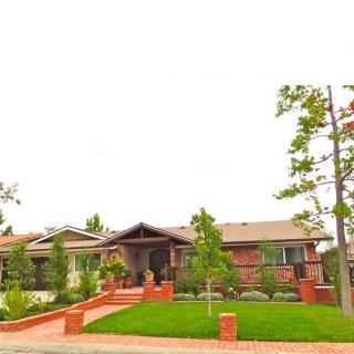 A brick residential house with a lush garden and driveway.