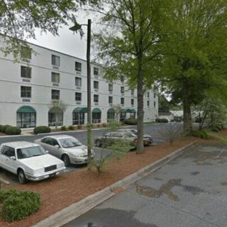 A view of a multi-story building with a parking lot and several cars surrounded by trees.
