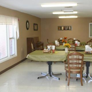 A neatly arranged dining room with multiple tables and chairs, featuring simple decor and ample lighting.