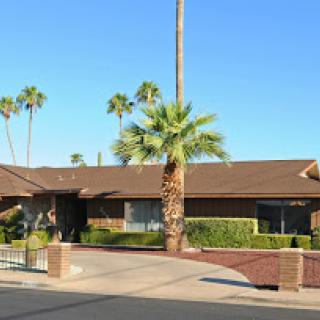 A sunny day showcasing a beautiful single-story house surrounded by palm trees.