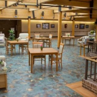 A spacious interior with wooden tables and chairs, decorated with plants and warm lighting.