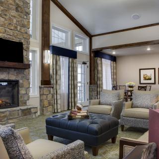A cozy living room featuring a stone fireplace, modern furniture, and large windows bringing in natural light.
