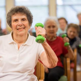 A group of seniors participating in a fitness class, lifting small dumbbells indoors.