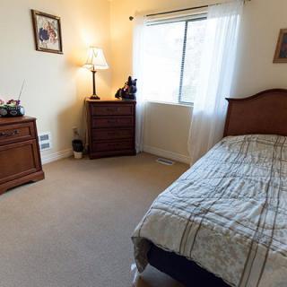 A cozy bedroom interior with a neatly made bed, two wooden dressers, a lamp, and a window with curtains.