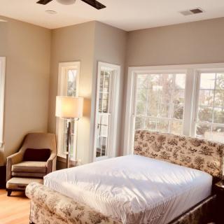 A bright and cozy bedroom with a large bed, armchair, and ample natural light streaming through windows.