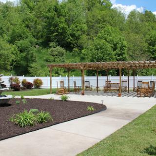A tranquil outdoor space featuring a patio with furniture, surrounded by lush greenery and a pergola.