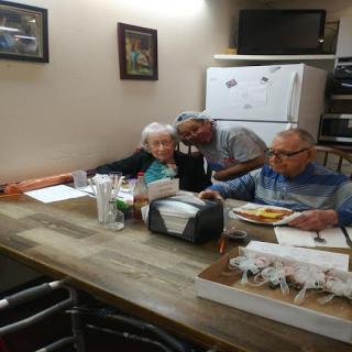 A warm moment shared among elderly individuals at a kitchen table, engaged in conversation and reviewing documents.