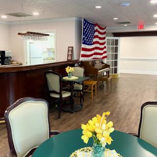 An interior view of a facility's dining or lobby area with tables, chairs, and an American flag displayed on the wall.