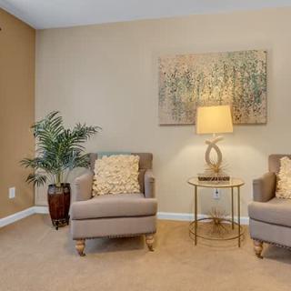 A cozy living room setup featuring two chairs, a lamp on a side table, and decorative artwork on the wall.