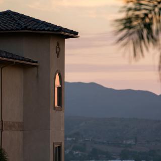 A picturesque view of a house at sunset with mountains in the background.