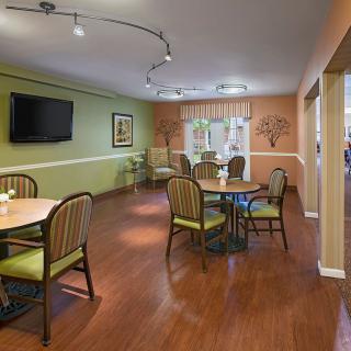 A cozy dining area with wooden floors, featuring several tables and chairs, a mounted television, and ambient lighting.