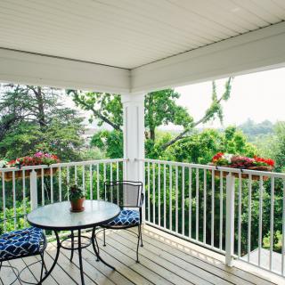 A cozy balcony with a round table and two chairs, surrounded by lush greenery.