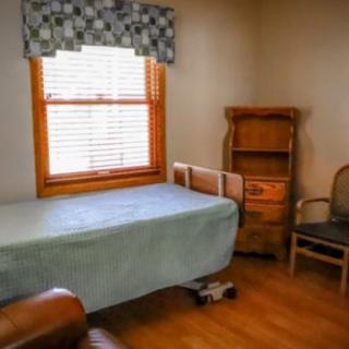 A small bedroom with minimal furnishings, featuring a bed, wooden shelves, and a window with blinds.