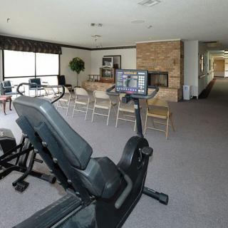 A fitness room featuring an exercise bike, chairs, and a television in a well-lit area with large windows.