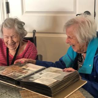 Two elderly women sharing a joyful moment as they look through a photo album.