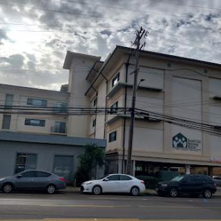 An urban scene featuring a multi-story building and parked cars against a cloudy sky.