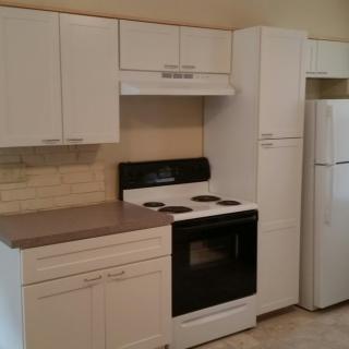 A modern kitchen setup with white cabinets, a stove, and a refrigerator.