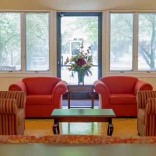 A cozy living room with two red armchairs, a central table, and large windows letting in natural light.
