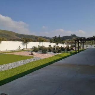 A scenic garden view with a pathway bordered by trees and distant mountains under a clear sky.