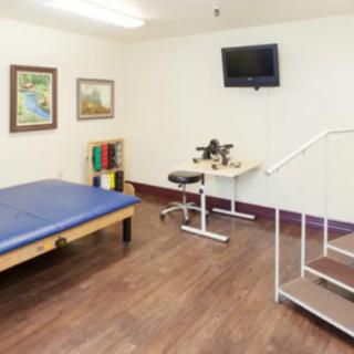 A physical therapy room equipped with a massage table, exercise equipment, and therapy stairs.