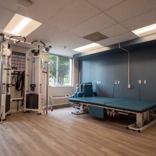 A rehabilitation room equipped with exercise machinery and a treatment table.