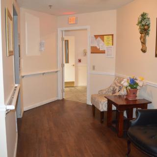 A hallway with wooden flooring, featuring a small seating area and decor along the walls.